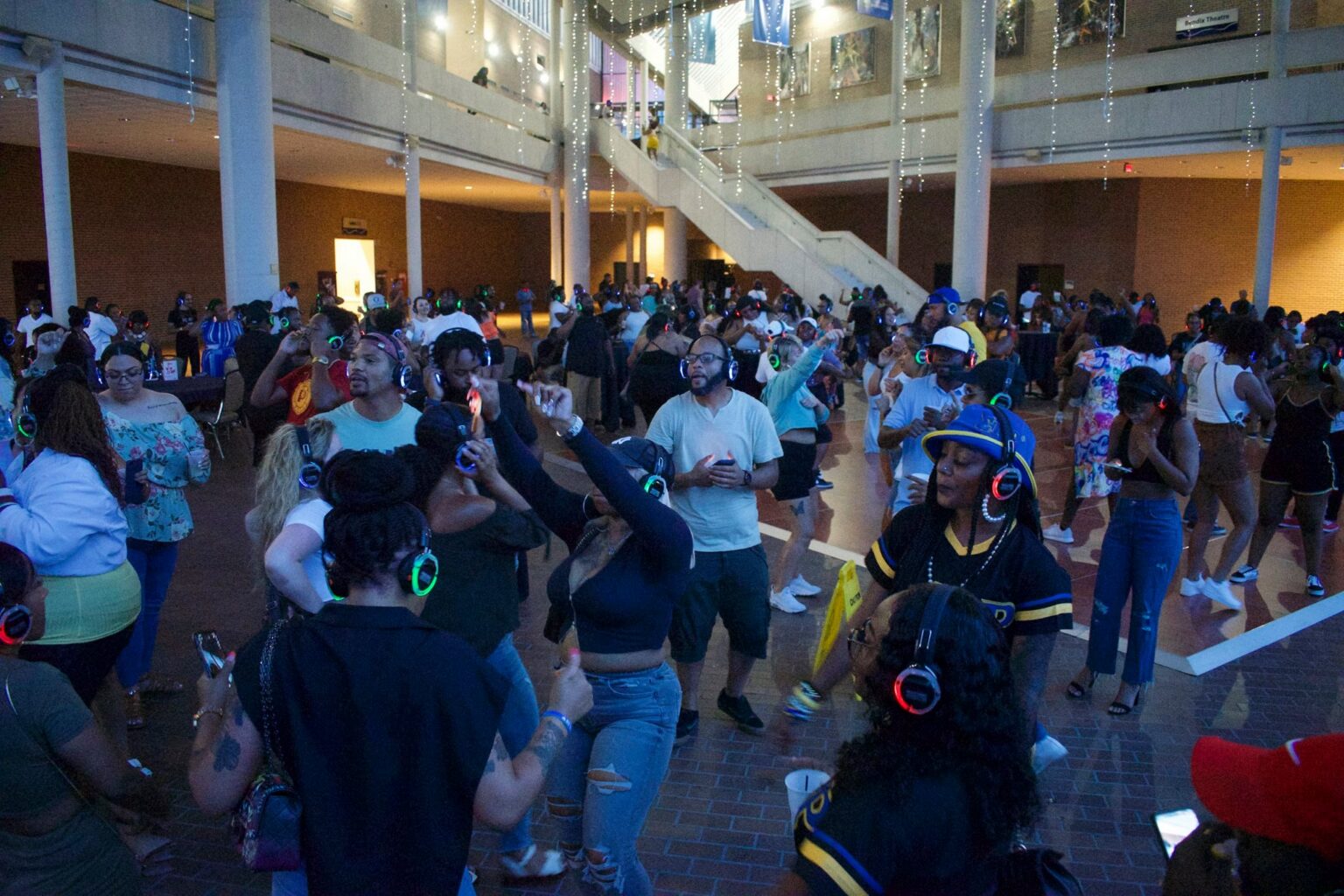 A large group of people wearing headphones dancing in a large open space.